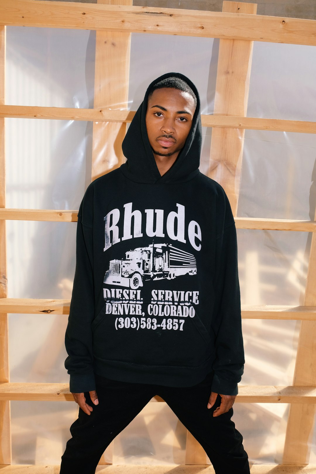 a-man-standing-in-front-of-a-wooden-wall-wearing-a-black-hoodie-m0uerdyo7-m