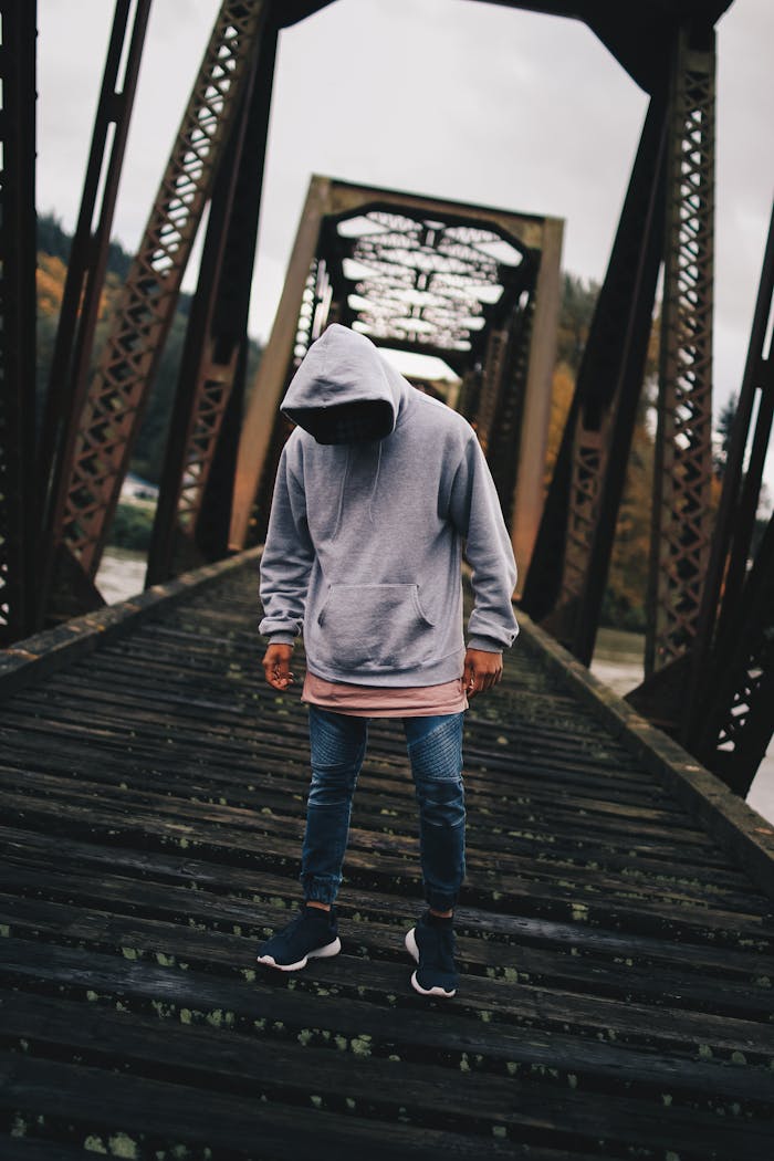 social-feed-img-02 Man in hoodie on a rustic urban bridge during daylight, showcasing casual street fashion.